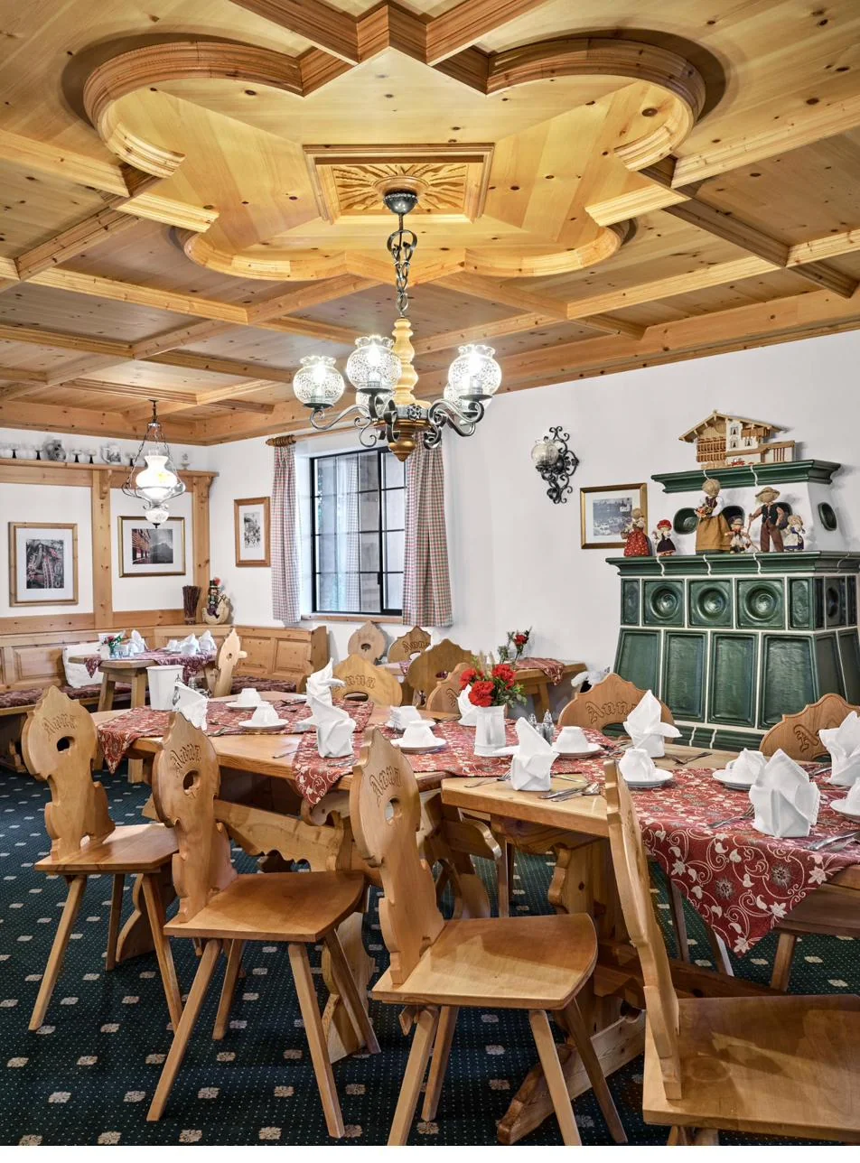The Pension Anna dining room — hand-carved 'Anna' chairs, ornate coffered pine ceiling, and green tiled Kachelofen stove